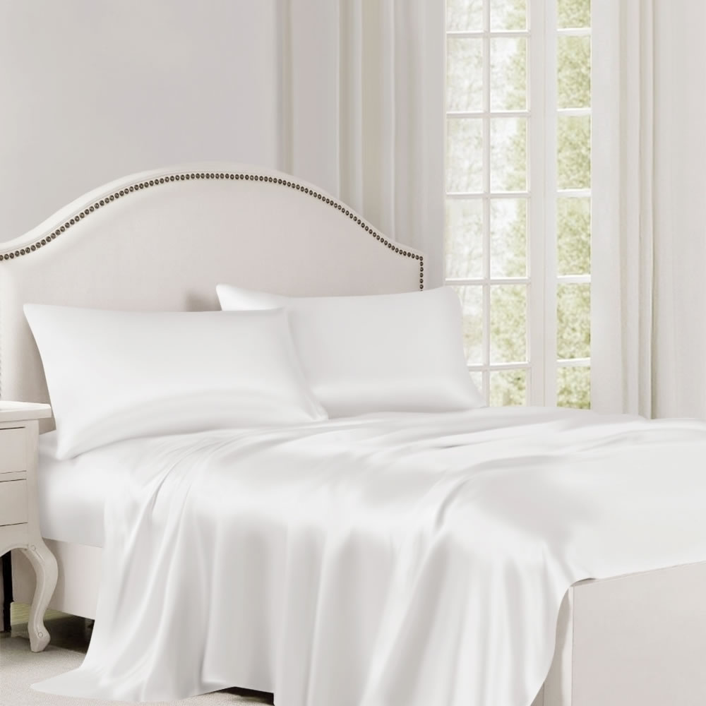 A bed made up in white mulberry silk sheets and pillowcases beside a bright window